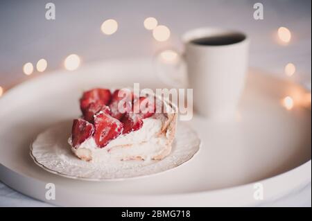 Delicious unbaked strawberry cake with cup of tea in bed on white tray closeup. Good morning. Birthday party. Stock Photo