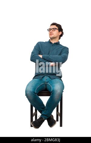 Full length portrait of confident businessman seated relaxed on a chair, wearing eyeglasses and keeps arms crossed, isolated on white background. Cont Stock Photo