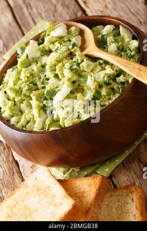 Tasty light avocado salad with eggs and green onions close-up in a bowl served with toasts on the table. vertical Stock Photo