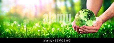 Hands Holding Crystal Earth In Lush Green Environment With Sunlight - Caring For The Environment Concept Stock Photo
