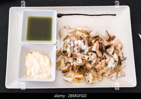 Grilled squid, grilled cuttlefish served as a Spanish tapa with garlic oil and a chopped garlic and parsley, top view sepia plancha Stock Photo