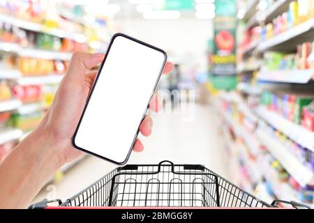 Man hand holding smartphone with shopping cart in supermarket ,Empty white screen smartphone for design advertising on mobile phone screen ezy replace Stock Photo
