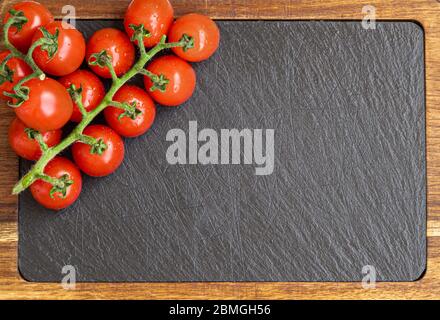 Fresh red cherry tomatoes over a black slate board with space for text Stock Photo