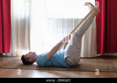 Caucasian man in yoga pose laying on back with legs up using belt Stock Photo