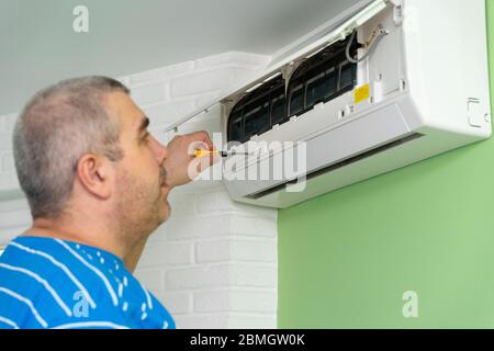 Male technician repairing and diagnosing air conditioners. Opening the cover and disassembling the housing Stock Photo