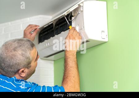 Male technician - repair and diagnostics of air conditioners. Opening the cover and removing the display for repair Stock Photo