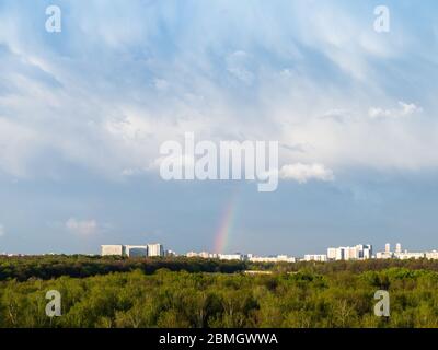 blue rainy clouds and rainbow over city on sunny spring day Stock Photo