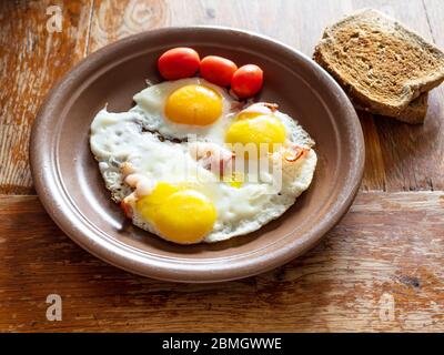 three fried eggs with bacon on brown ceramic plate on shabby wooden table at home kitchen Stock Photo