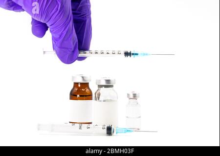 Pharmaceutical Scientist picking up a syringe. Coronavirus vaccine research. Medicine vials in white background . Stock Photo