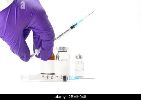 Pharmaceutical Scientist picking up a syringe. Coronavirus vaccine research. Medicine vials in white background . Stock Photo