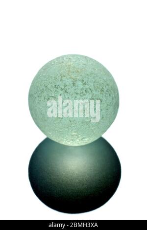 Close up still life of a chipped and damaged pale blue glass marble and the shadow it casts in directional sunlight against a white background. Stock Photo