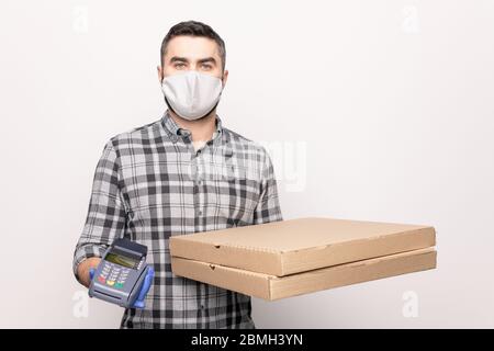 Young male courier from cafe holding two large square carton boxes and payment machine while delivering you ordered pizza Stock Photo