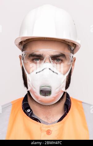 Head of young male engineer or foreman in respirator, protective eyeglasses, hardhat and workwear looking at you on white background Stock Photo