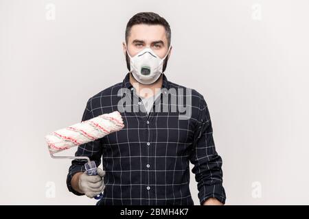 Young serious male painter with roller going to paint walls of room inside new house while standing in front of camera on white background Stock Photo