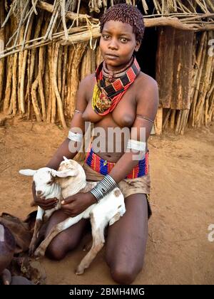 A pretty young girl with two kids on her knees in front of a hut in the village Gabo. Stock Photo
