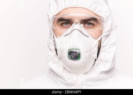 Young contemporary male scientist in protective eyewear, respirator and coveralls looking at you during work over new vaccine Stock Photo