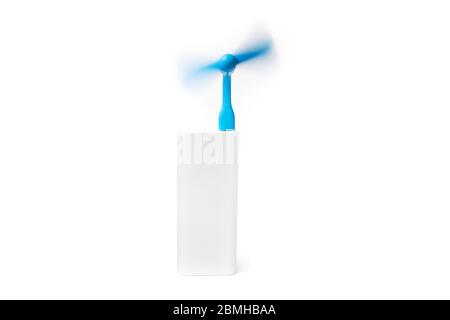 A portable blue usb fan is spinning powered by a silver power bank isolated on a white background. Stock Photo