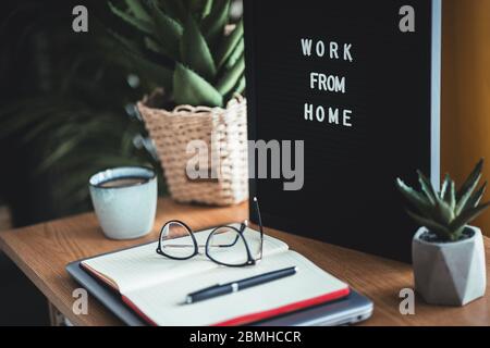 Background image of business office with laptop and supplies on wooden desk, focus on black hard rim glasses in foreground. Work from home concept Stock Photo