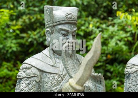 Standing stone statue with weapon at the buddhist Temple of Ten Thousand Buddhas in Pai Tau, New Territories, Hong Kong Stock Photo