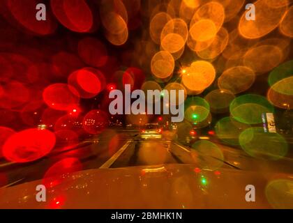 Colorful view through the rainy front window of a car while its waiting at a traffic jam. Stock Photo