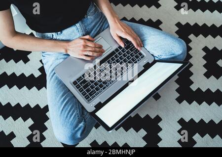 Working home concept - girl sitting on the floor while working at laptop. Stock Photo