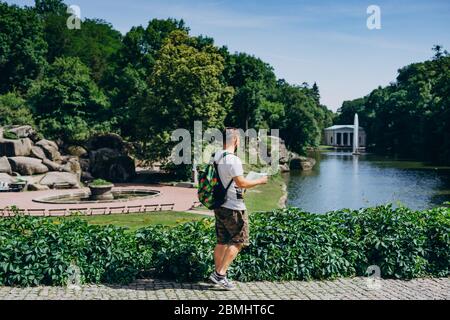 Sofia Park, Ukraine. Man with a backpack with a tourist map in a landscape park in summer. Guy in a T-shirt with a tourist map on the background of th Stock Photo