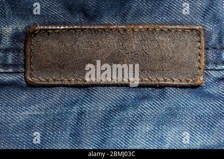 old weathered and cracked blank leather label on blue denim cloth - close-up with selective focus and partial blur. long tag Stock Photo