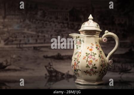 Closeup of a beautiful old coffee pot made of porcelain, painted with flowers standing on a reflective table Stock Photo
