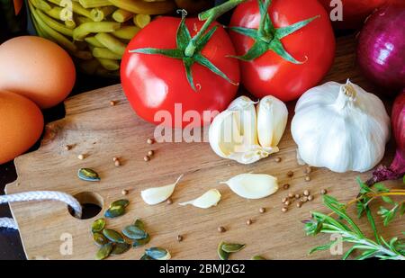 Composition of vegetables, herbs, spices, seeds and eggs on a wooden cutting board. Visible are: eggs, tomatos, garlic, red onions, tymus, rosemary, p Stock Photo