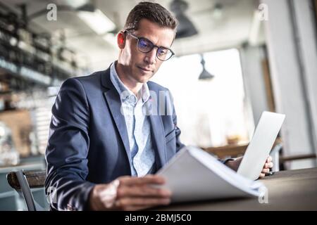 Businessman wearing glasses sits in a cafe, reading. Stock Photo