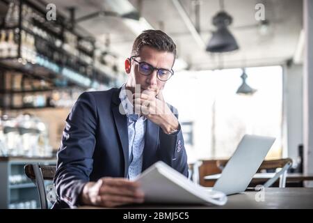 Focused male reading a paper sits in an empty restaurant or cafe in his office clothes. Stock Photo