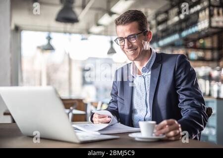 Entrepreneur smiles at the computer screen while having a coffee during a business break in a vintage restaurant. Stock Photo