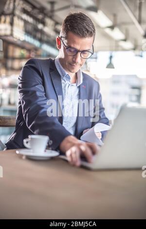 Elegantly dressed man works focused in a cafeteria wearing glasses. Stock Photo