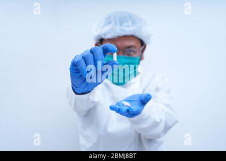 scientist with protective mask holding a pill with fingers in gloves in pharmaceutical research laboratory Stock Photo