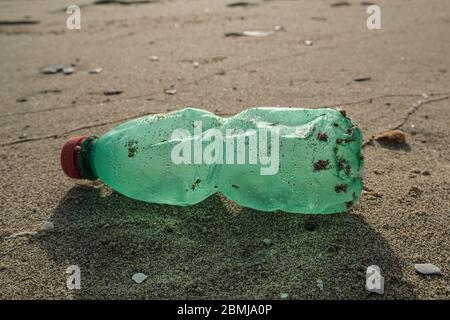 Green Plastic trash bottle and seashell on sea shore,polluted ecosystem concept Stock Photo