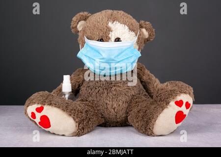 portrait of a brown teddy bear dressed in a blue medical mask with antiseptic on a dark background. isolation symbol, quarantine, covid-19, stay in ho Stock Photo