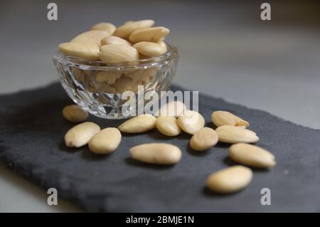 A glass bowl with raw peeled almonds on a black slate board and neutral background Stock Photo