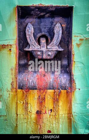 Rusty purple color anchor hanging on a rusted green and orange boat hull Stock Photo