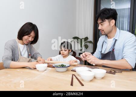 Young Asian mom and dad making dumplings with daughter Stock Photo