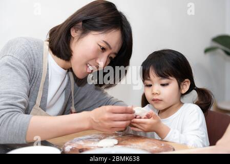 Young Asian mom and dad making dumplings with daughter Stock Photo