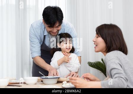 Young Asian mom and dad making dumplings with daughter Stock Photo