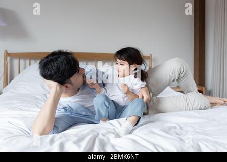 Young Asian dad is unpacking gifts on bed with daughter Stock Photo