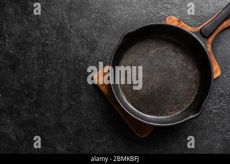 Empty cast iron frying pan for cooking on black background, top view, copy space. Cooking concept background with black pan. Stock Photo
