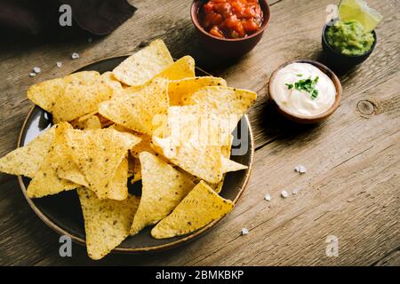 Mexican Corn Chips Nachos and set of traditional dips on wooden table, copy space. Tortilla or Nacho Chips with sauces for snack. Stock Photo