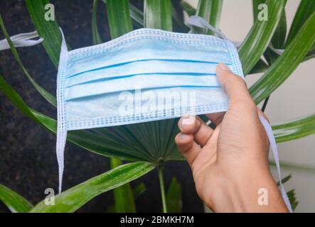 Man's hand reaching for safety mask,man holding protective mask. A surgical mask on plant background. Stock Photo