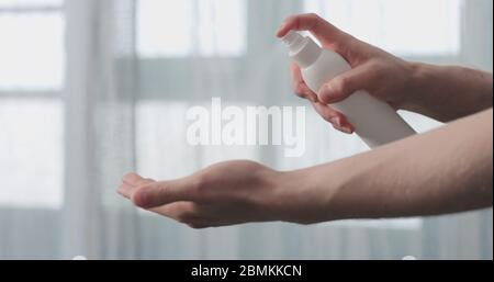 man spraying sanitizer on his hands standing in front of the window closeup Stock Photo