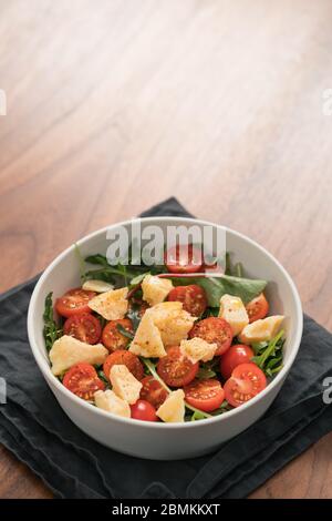 salad with cherry tomatoes, mixed grens and cheese in white bowl on wood table Stock Photo