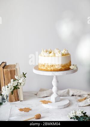 Homemade Russian layered cake with honey Medovik with cream and merengue on the top. White flowers, autumn leaves, old books nearby on the white table Stock Photo
