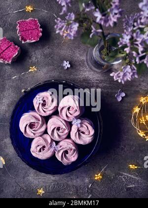 Atmospheric violet sweet homemade Zephyr or Marshmallow from black currant near lilac flowers and magic stars lights on dark background top view Stock Photo