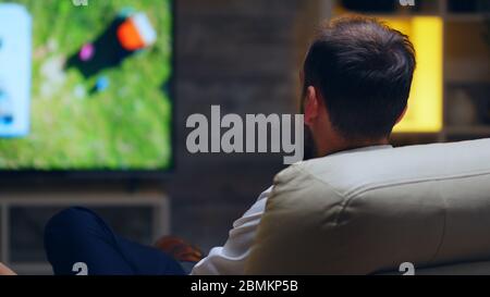 Back view of businessman taking a sip of beer while watching tv. Stock Photo